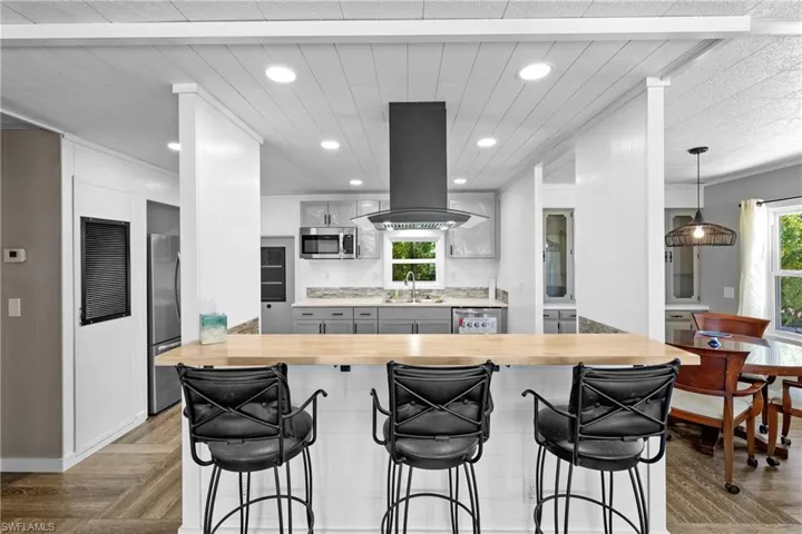 Kitchen with wooden counters, appliances with stainless steel finishes, a sink, island range hood, and recessed lighting