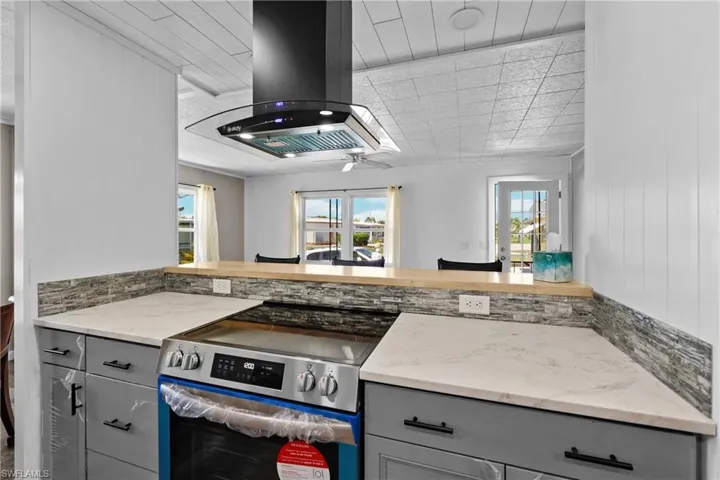 Kitchen with stainless steel electric stove, gray cabinets, and island exhaust hood