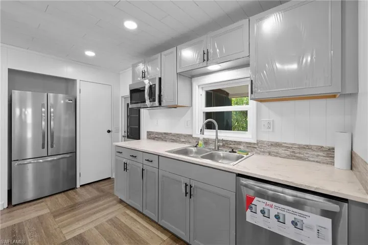 Kitchen with stainless steel appliances, a sink, gray cabinetry, light stone counters, and recessed lighting