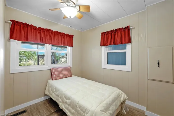 Bedroom featuring wood finished floors, baseboards, ceiling fan, and a decorative wall