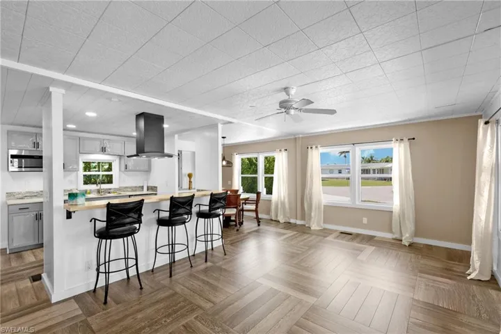 Kitchen featuring island exhaust hood, gray cabinets, light countertops, stainless steel microwave, and a breakfast bar