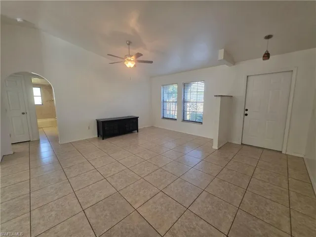 Unfurnished living room with lofted ceiling, arched walkways, ceiling fan, and light tile patterned floors