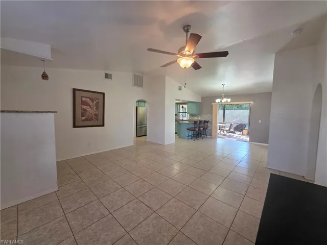 Unfurnished room with arched walkways, lofted ceiling, light tile patterned floors, a ceiling fan, and a chandelier