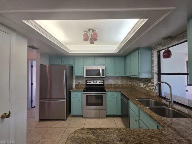 Kitchen with stainless steel appliances, a raised ceiling, dark stone countertops, and decorative backsplash