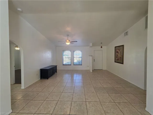 Empty room featuring arched walkways, ceiling fan, light tile patterned floors, and vaulted ceiling