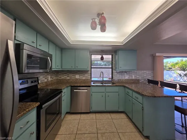 Kitchen featuring stainless steel appliances, a tray ceiling, dark stone counters, green cabinetry, and light tile patterned flooring