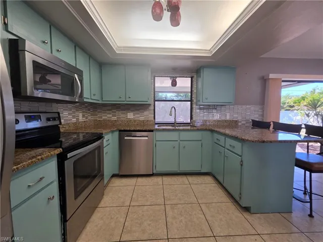 Kitchen featuring stainless steel appliances, a breakfast bar, a tray ceiling, and dark stone counters