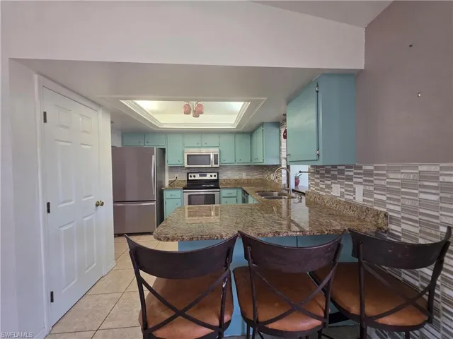 Kitchen featuring a kitchen breakfast bar, stainless steel appliances, a raised ceiling, a peninsula, and dark stone countertops
