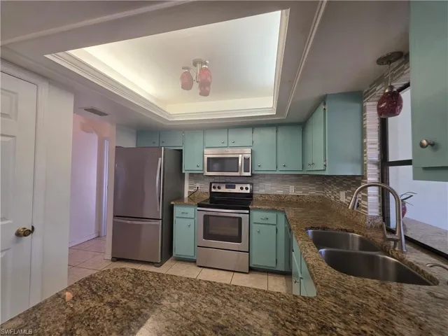 Kitchen with a raised ceiling, appliances with stainless steel finishes, dark stone countertops, light tile patterned floors, and decorative backsplash