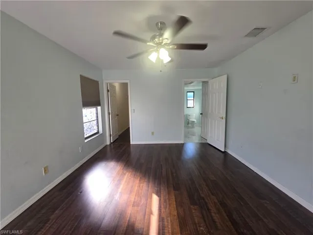 Unfurnished bedroom with multiple windows, dark wood finished floors, a ceiling fan, and ensuite bathroom