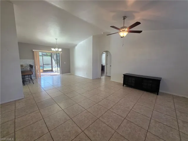 Unfurnished living room with a chandelier, lofted ceiling, a ceiling fan, light tile patterned floors, and arched walkways