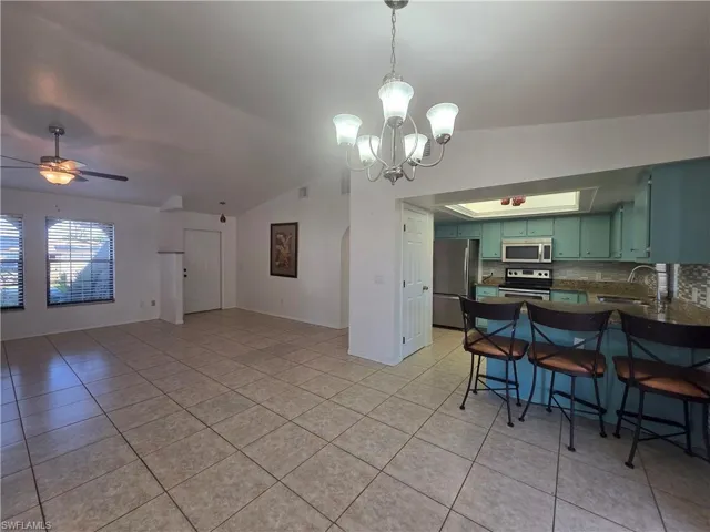 Kitchen featuring appliances with stainless steel finishes, a breakfast bar area, decorative light fixtures, light tile patterned floors, and lofted ceiling