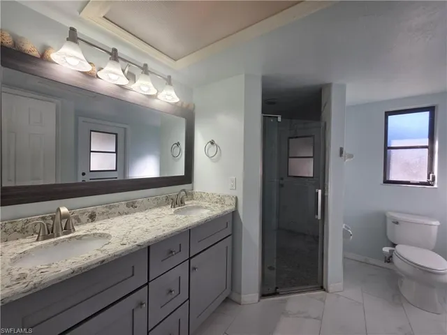 Full bath featuring double vanity, a shower stall, light marble finish floors, and crown molding