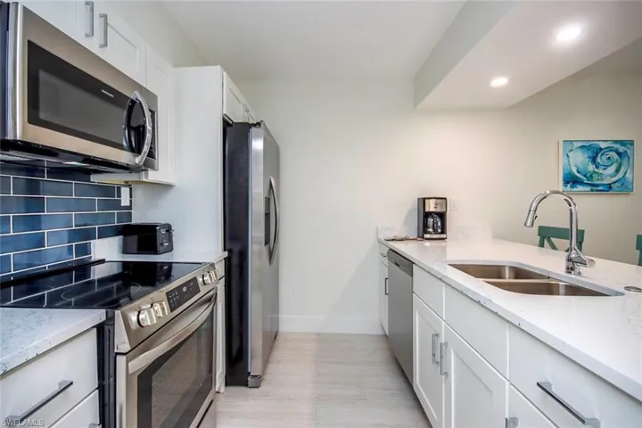 Kitchen with appliances with stainless steel finishes, light stone counters, tasteful backsplash, recessed lighting, and white cabinets