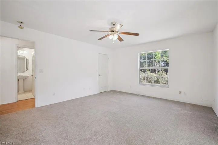 Another view of the primary bedroom featuring light colored carpet and ceiling fan