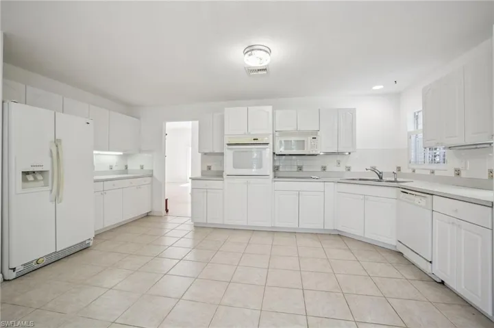 Kitchen with white appliances, backsplash, white cabinets, and light countertops
