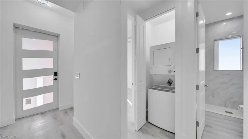 Washroom with stacked washer / dryer and light wood finished floors