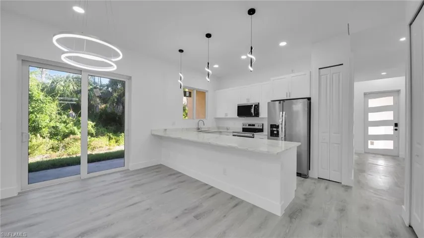 Kitchen featuring a peninsula, stainless steel appliances, light stone counters, white cabinets, and hanging light fixtures