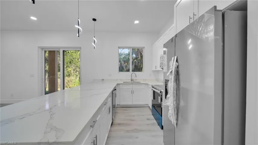 Kitchen featuring stainless steel appliances, white cabinetry, light stone countertops, hanging light fixtures, and recessed lighting