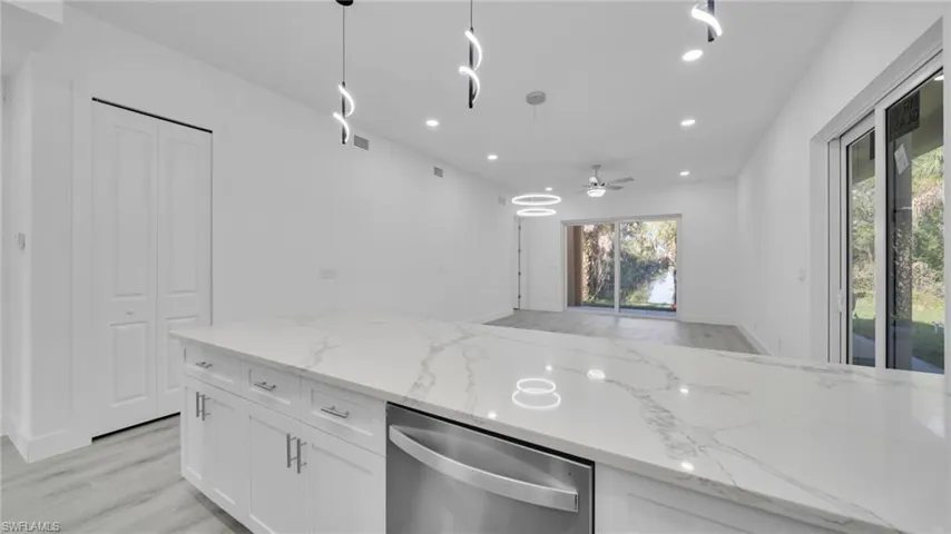 Kitchen with light wood-type flooring, light stone countertops, white cabinetry, stainless steel dishwasher, and recessed lighting