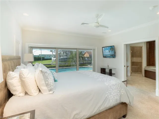 Tiled bedroom with ceiling fan, ornamental molding, connected bathroom, and access to outside