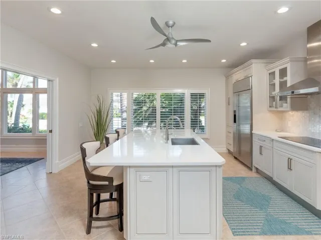 Kitchen featuring sink, a breakfast bar, wall chimney exhaust hood, an island with sink, and built in refrigerator