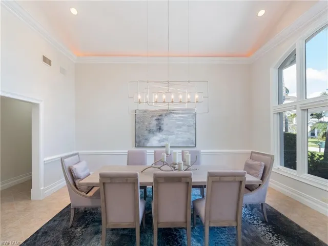Tiled dining space with ornamental molding, high vaulted ceiling, and a chandelier