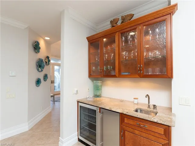 Bar featuring wine cooler, light stone countertops, sink, and crown molding