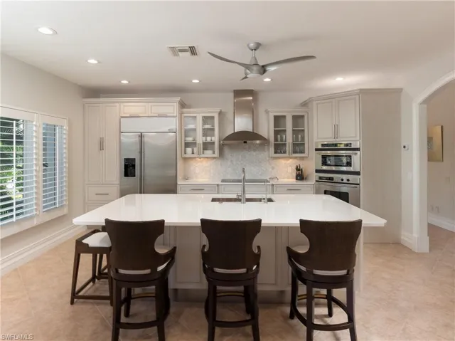 Kitchen featuring stainless steel appliances, sink, wall chimney range hood, a breakfast bar, and a large island with sink