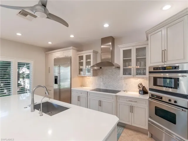 Kitchen with stainless steel appliances, light tile patterned flooring, sink, tasteful backsplash, and wall chimney exhaust hood