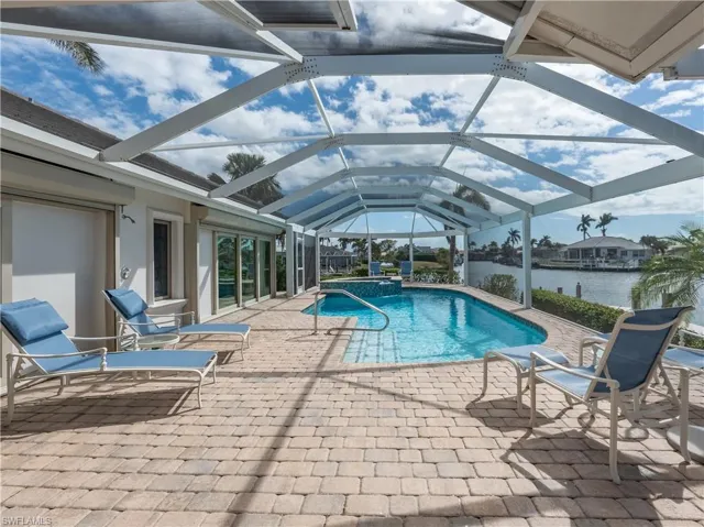 View of pool with a lanai, a water view, a hot tub, and a patio area
