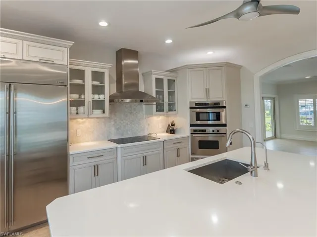 Kitchen with sink, appliances with stainless steel finishes, crown molding, white cabinets, and wall chimney range hood