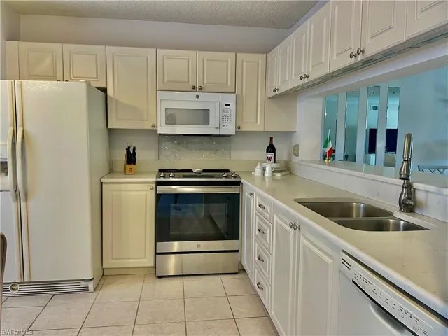 Kitchen with white appliances, light tile patterned floors, a textured ceiling, white cabinetry, and light stone countertops