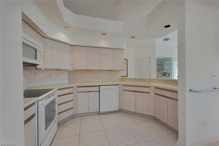 Kitchen with backsplash, white appliances, a raised ceiling, and light cabinets