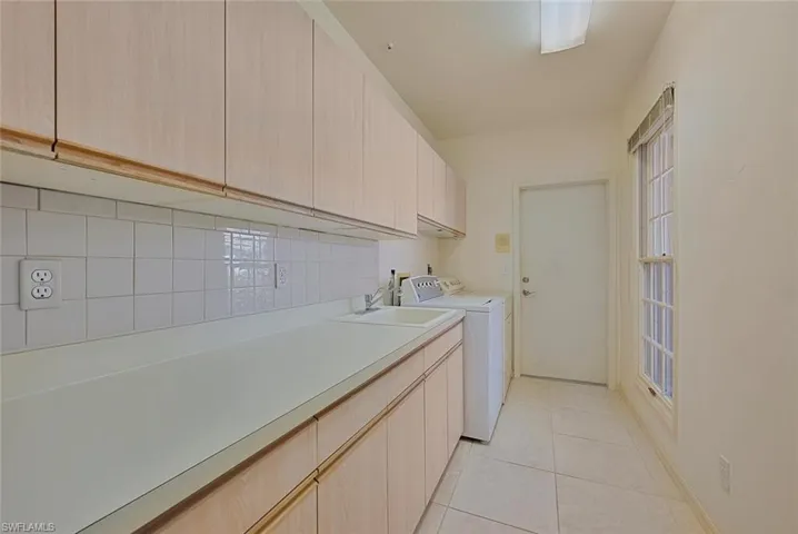 Spacious laundry area with light tile patterned flooring, cabinets, separate washer and dryer, and sink