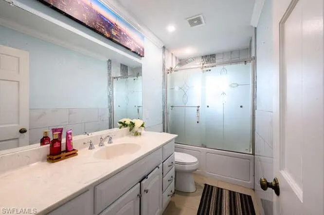 Full bathroom featuring tile patterned flooring, toilet, shower / bath combination with glass door, and vanity