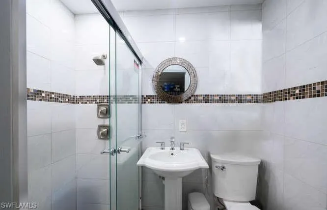 Bathroom featuring tile walls, toilet, sink, and an enclosed shower