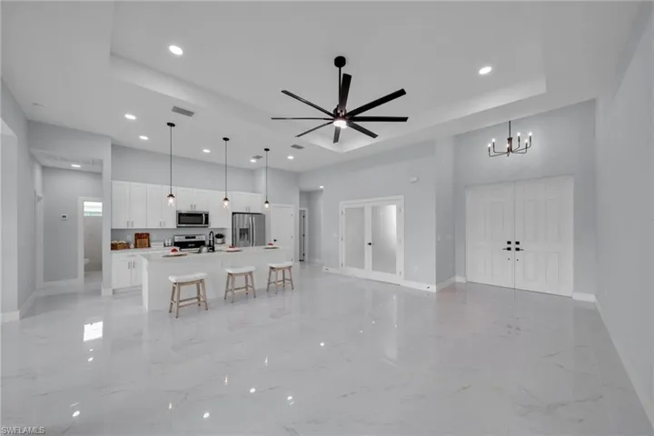 Living room featuring a tray ceiling, light marble finish floors, ceiling fan, and recessed lighting