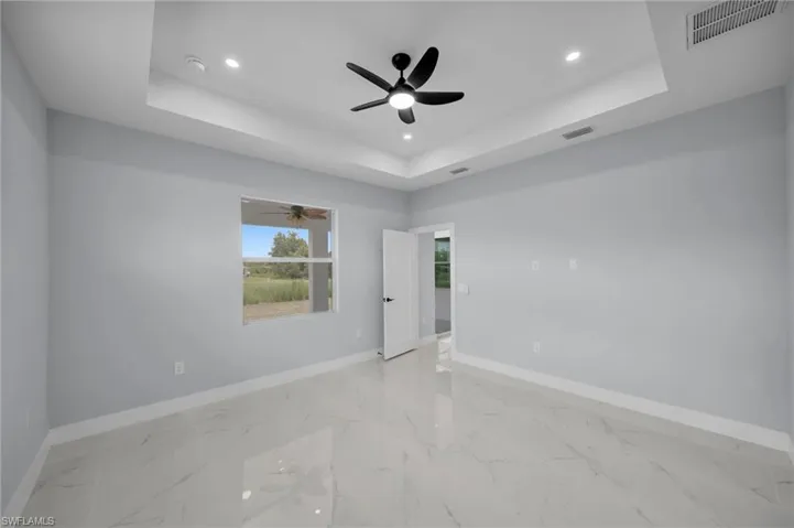 Empty room with a tray ceiling, light marble finish floors, recessed lighting, and ceiling fan