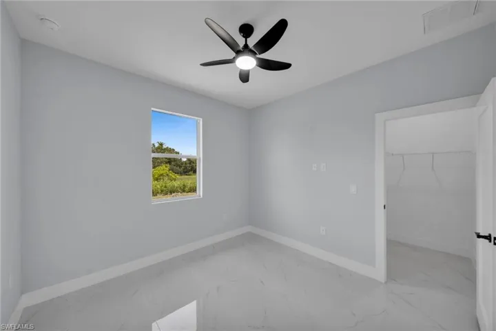 Unfurnished bedroom featuring light marble finish flooring, a spacious closet, and a ceiling fan