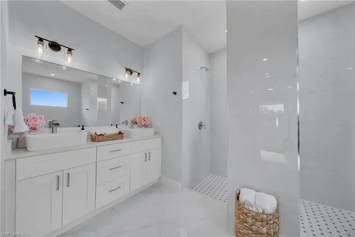 Full bath with double vanity, a marble finish shower, and light marble finish floors