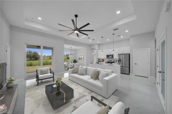 Living room with a tray ceiling, light marble finish flooring, ceiling fan, recessed lighting, and a chandelier