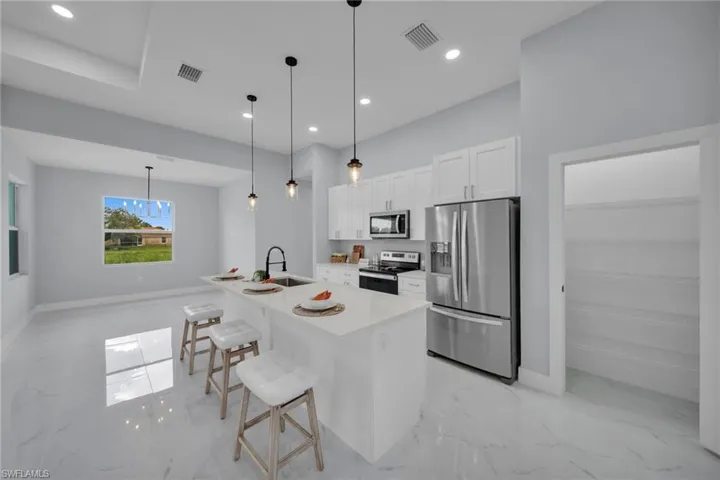 Kitchen featuring appliances with stainless steel finishes, white cabinets, a kitchen bar, light marble finish flooring, and a center island with sink