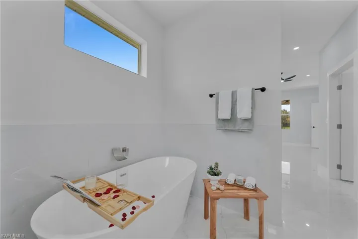 Bathroom featuring a soaking tub, marble finish flooring, recessed lighting, and a wainscoted wall