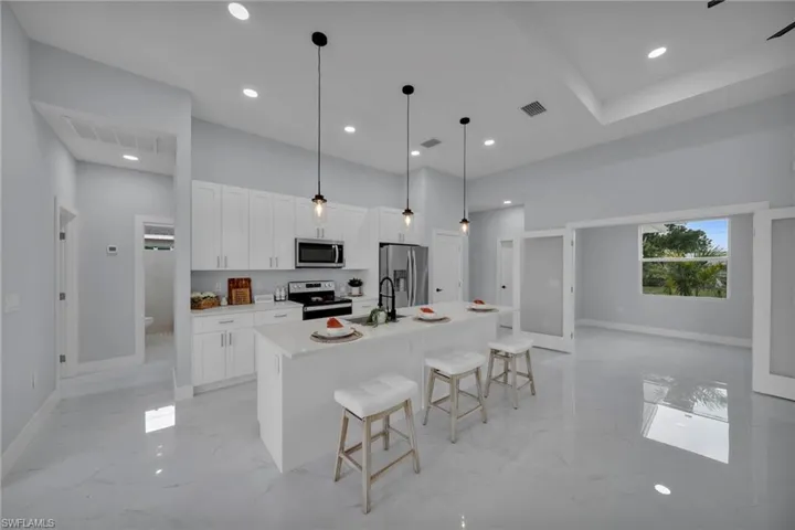 Kitchen with a kitchen breakfast bar, white cabinetry, a kitchen island with sink, stainless steel appliances, and pendant lighting