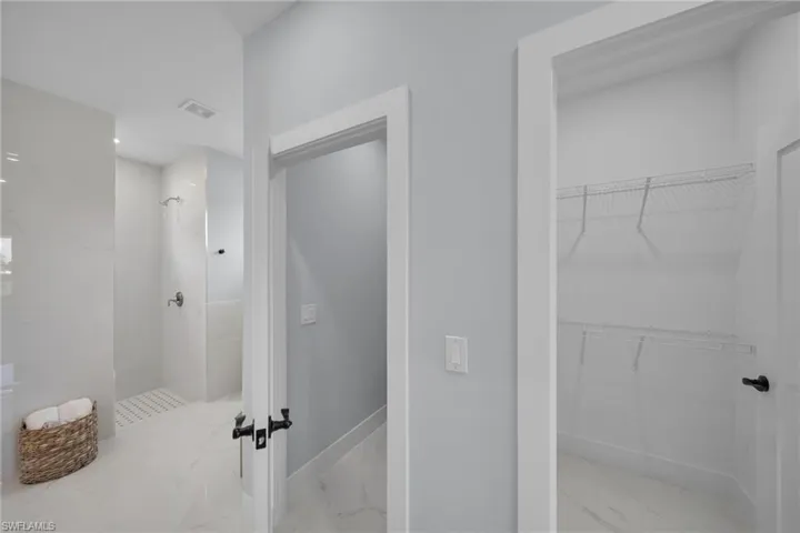 Full bath featuring a marble finish shower, light marble finish floors, and a walk in closet