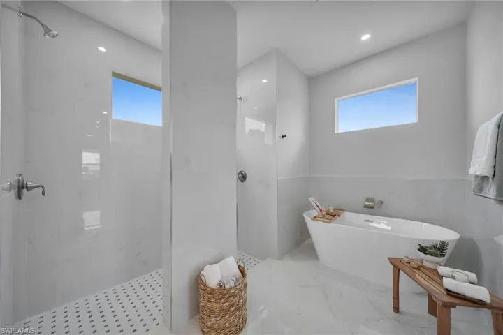 Bathroom featuring a marble finish shower, a freestanding tub, tile walls, plenty of natural light, and recessed lighting