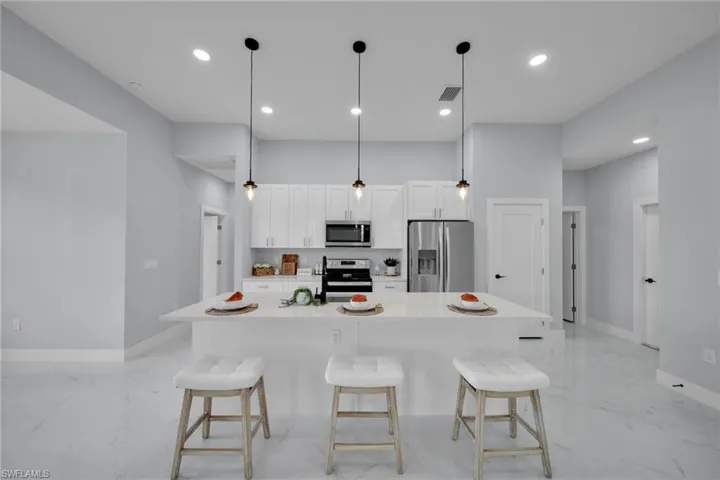 Kitchen featuring light marble finish floors, appliances with stainless steel finishes, white cabinetry, a breakfast bar, and a kitchen island with sink