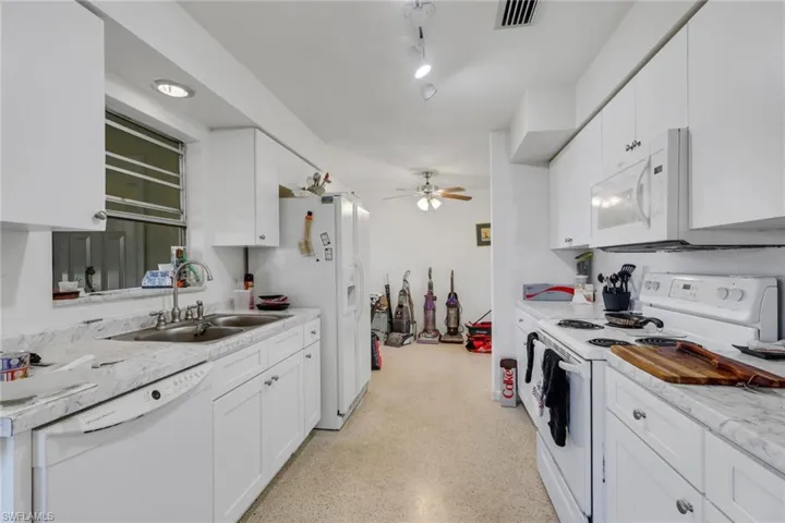 Kitchen with white appliances, light countertops, white cabinets, dark speckled floor, and ceiling fan