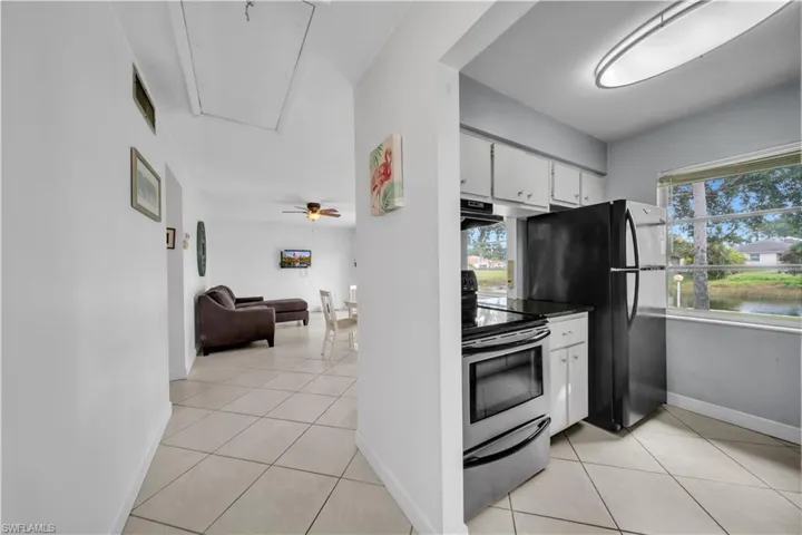 Kitchen with stainless steel range with electric cooktop, light tile patterned floors, white cabinets, dark countertops, and freestanding refrigerator